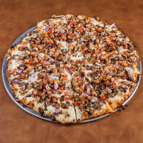 Mark & Monica's Family Pizza with chicken, mushrooms, red onions, and tomatoes on a metal pan.
